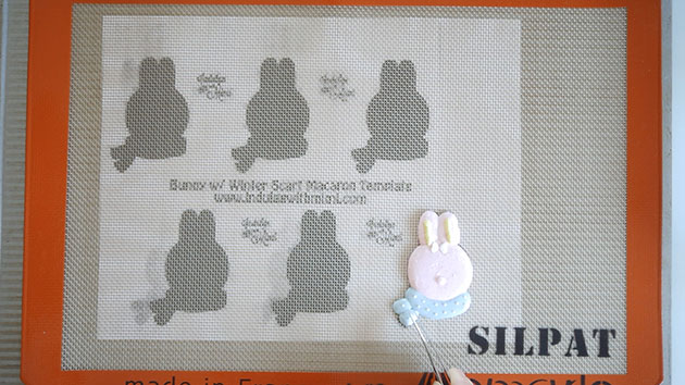 A bunny character macaron with multiple colors piped onto a silicone mat. 