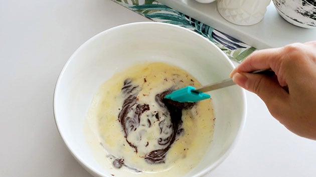 A spatula swirling a bowl of cream and chocolate. 