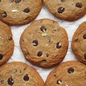 Large chocolate chip cookies with gold flakes laid out in a row on parchment paper.