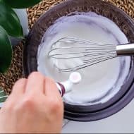 Hand adding food color into meringue.