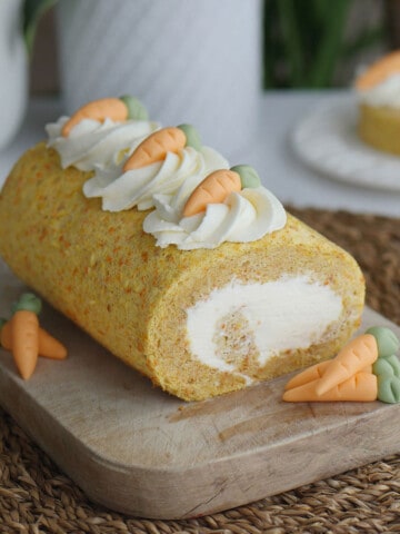 Carrot cake roll on a wooden cutting board flanked by fondant carrots.