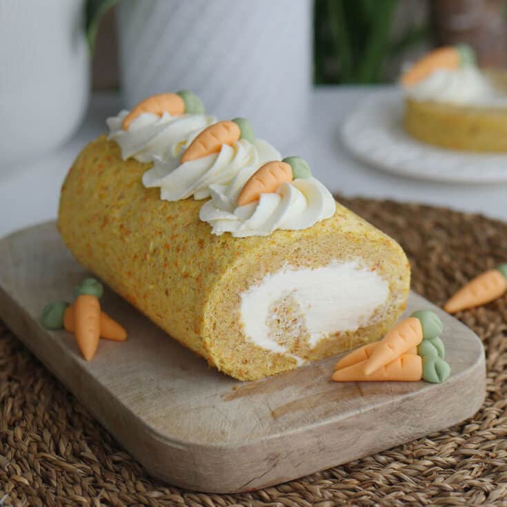 Carrot cake roll on a wooden cutting board flanked by fondant carrots.