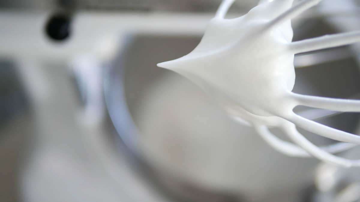 A whisk is shown with stiff peaked meringue hanging off it. 