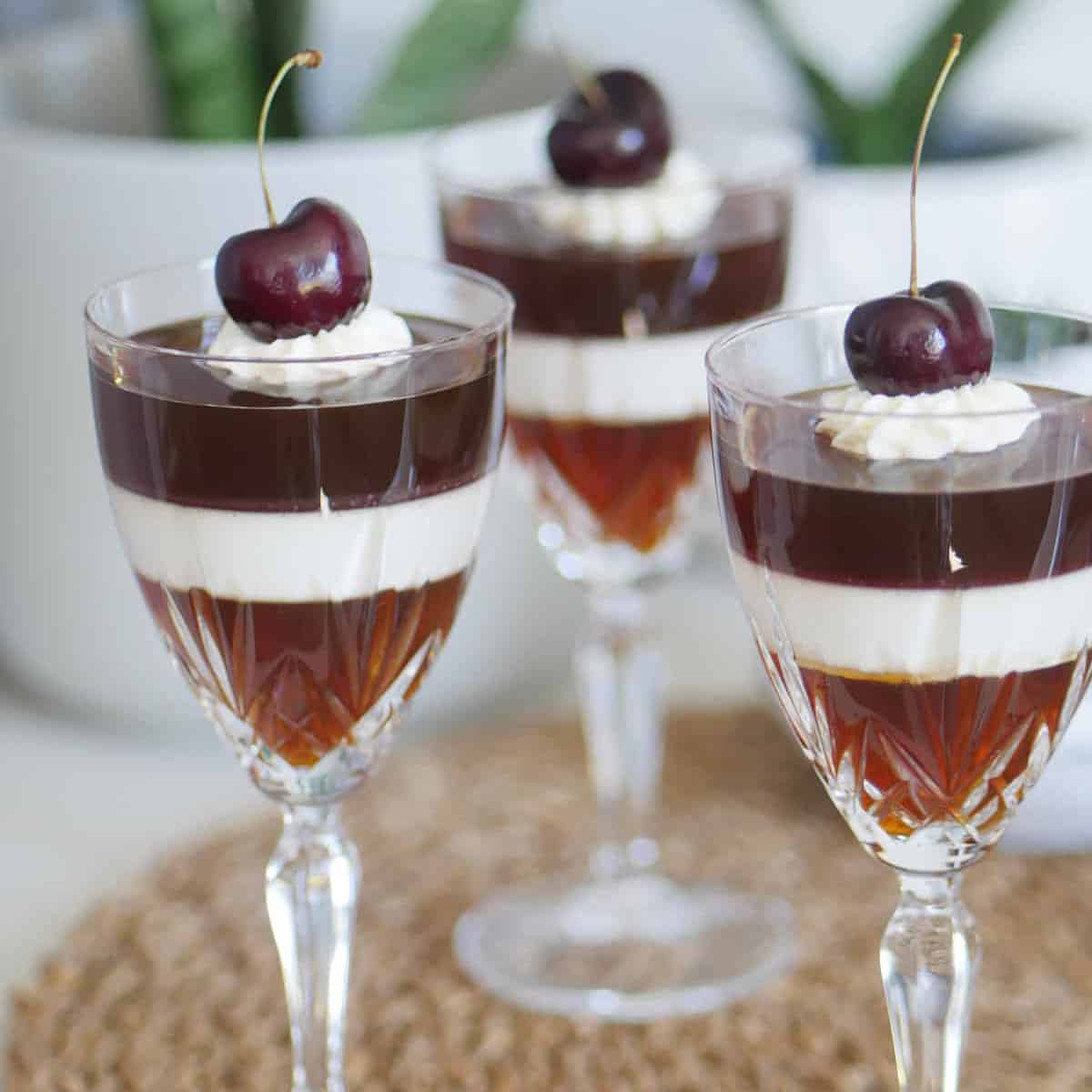 Close up of coffee jello in crystal glasses topped with whipped cream and cherries.