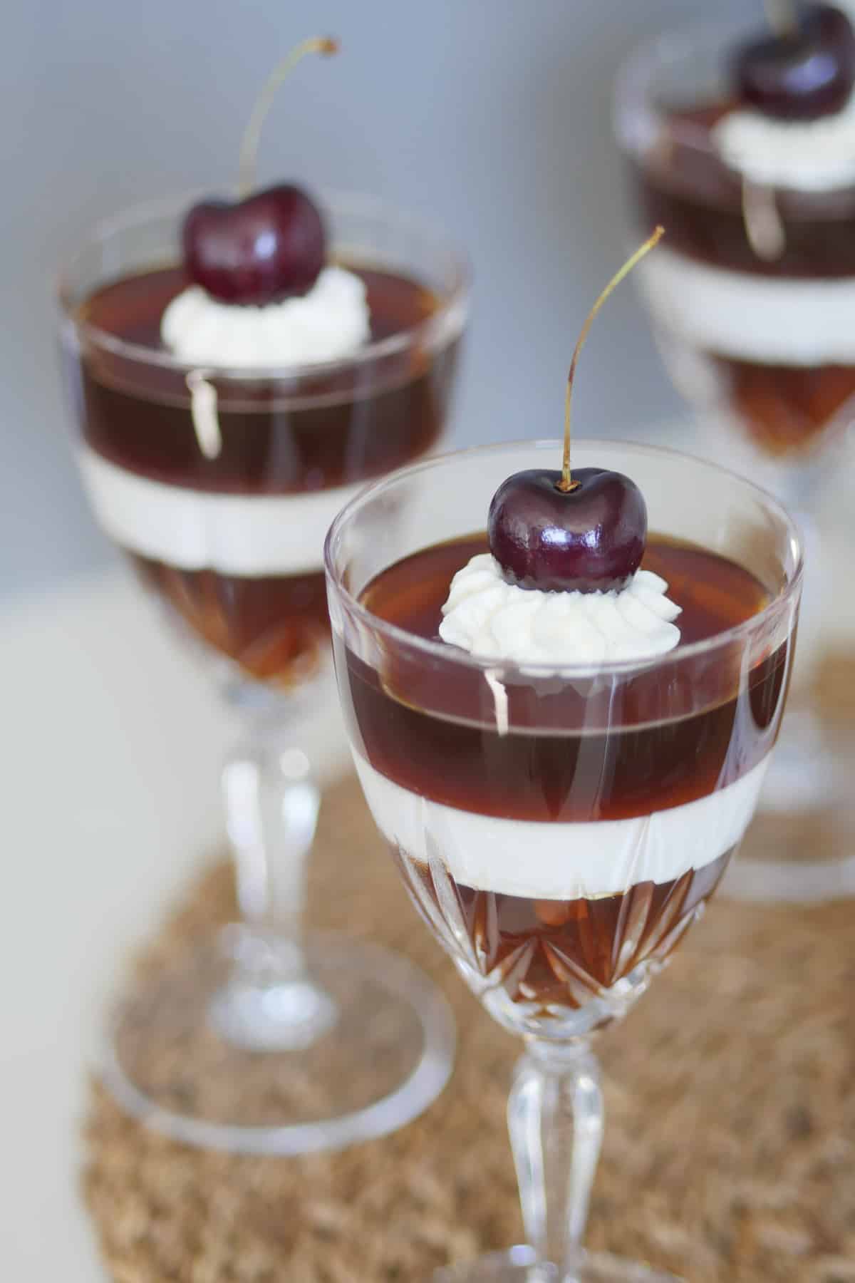 Close up view of a dessert topped with whipped cream and a dark red cherry.