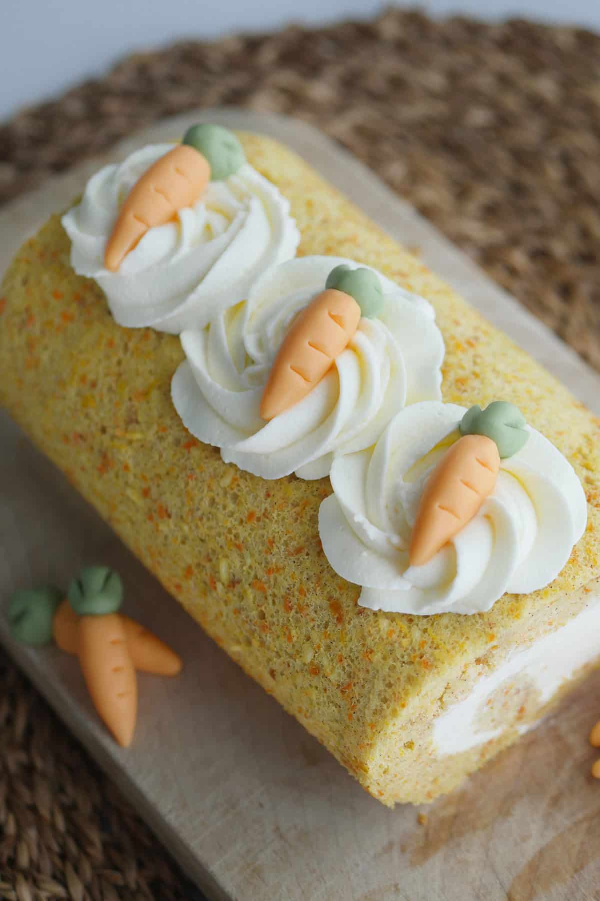 Close up of mascarpone cream piped into a swirl topped with fondant carrots on top of the carrot cake. 