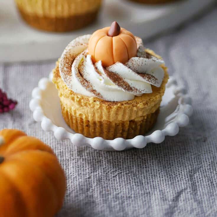 Close up of a fondant pumpkin on top of cheesecake and whipped cream.