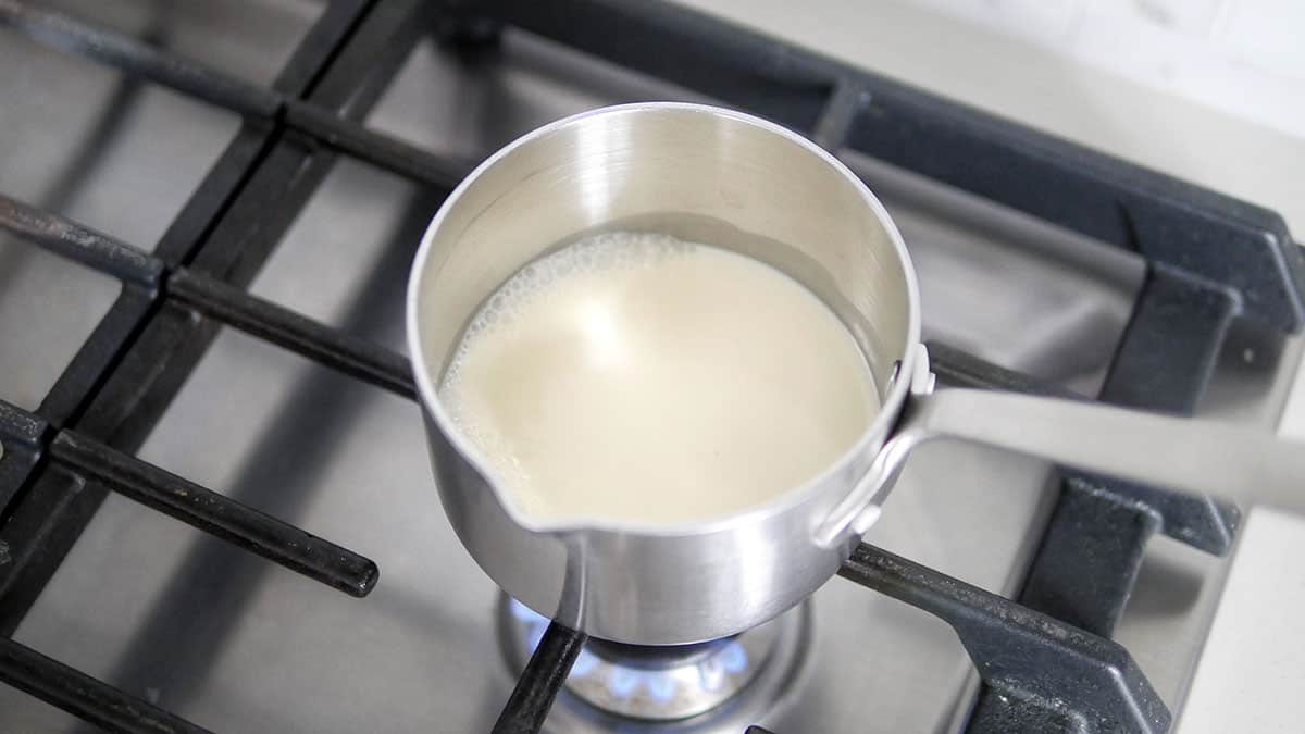 Cream being heated in a little sauce pan on a stovetop burner. 