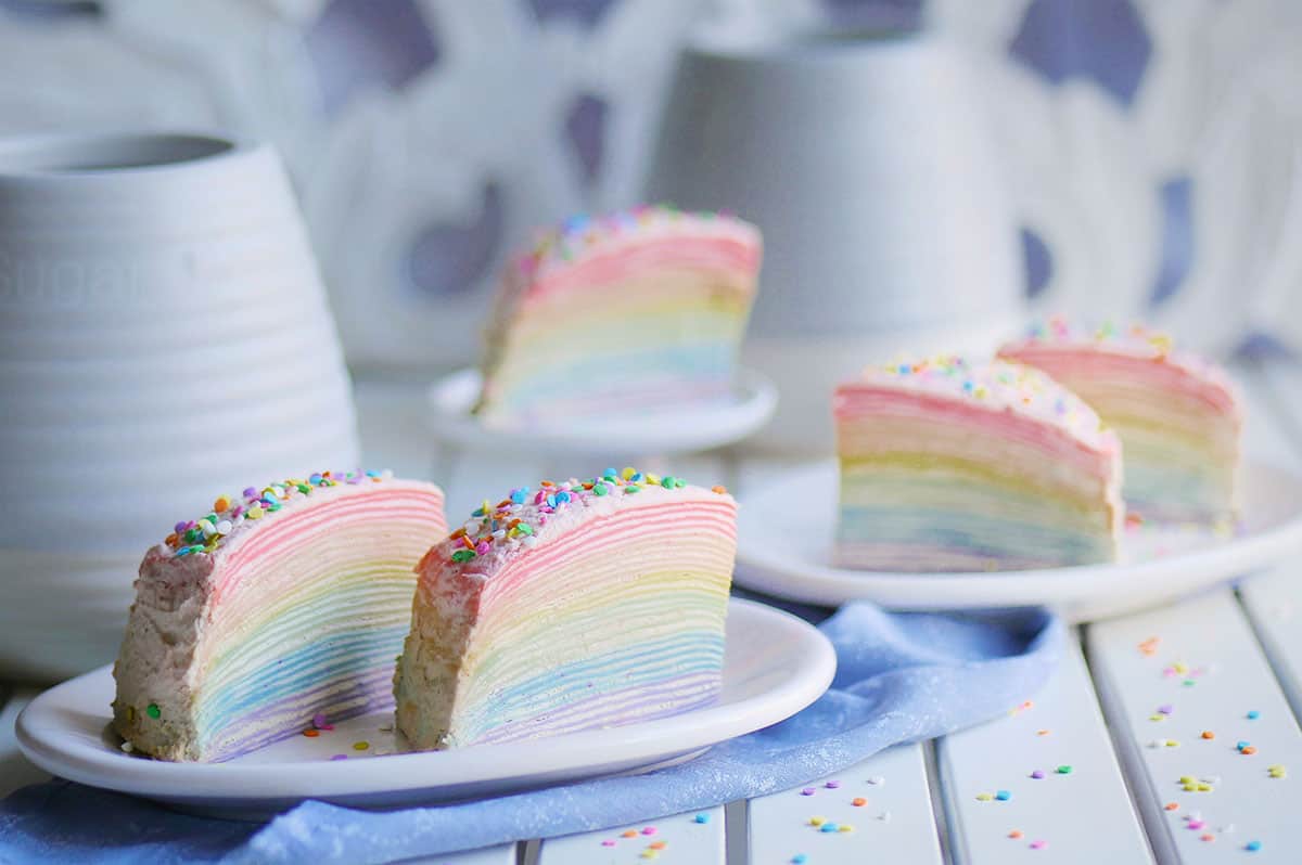 5 slices of crepe cake in rainbow colors laid out on a table with sprinkles scattered around. 