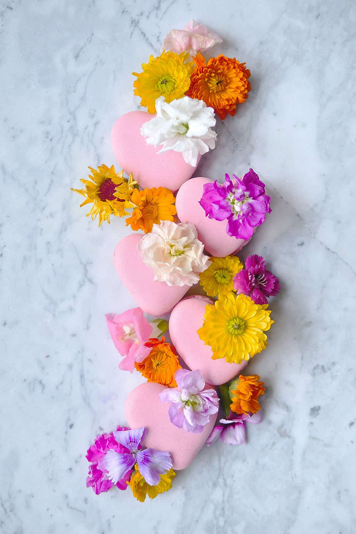 Lychee macarons in heart shapes topped with edible flowers. 