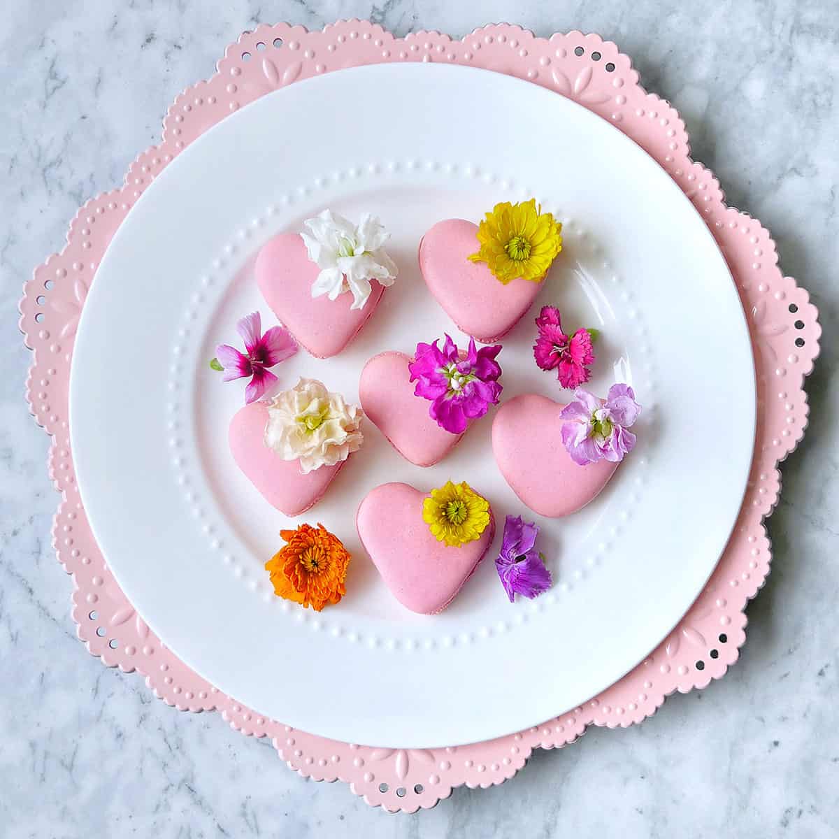 Heart macarons on a pink scalloped plate. 