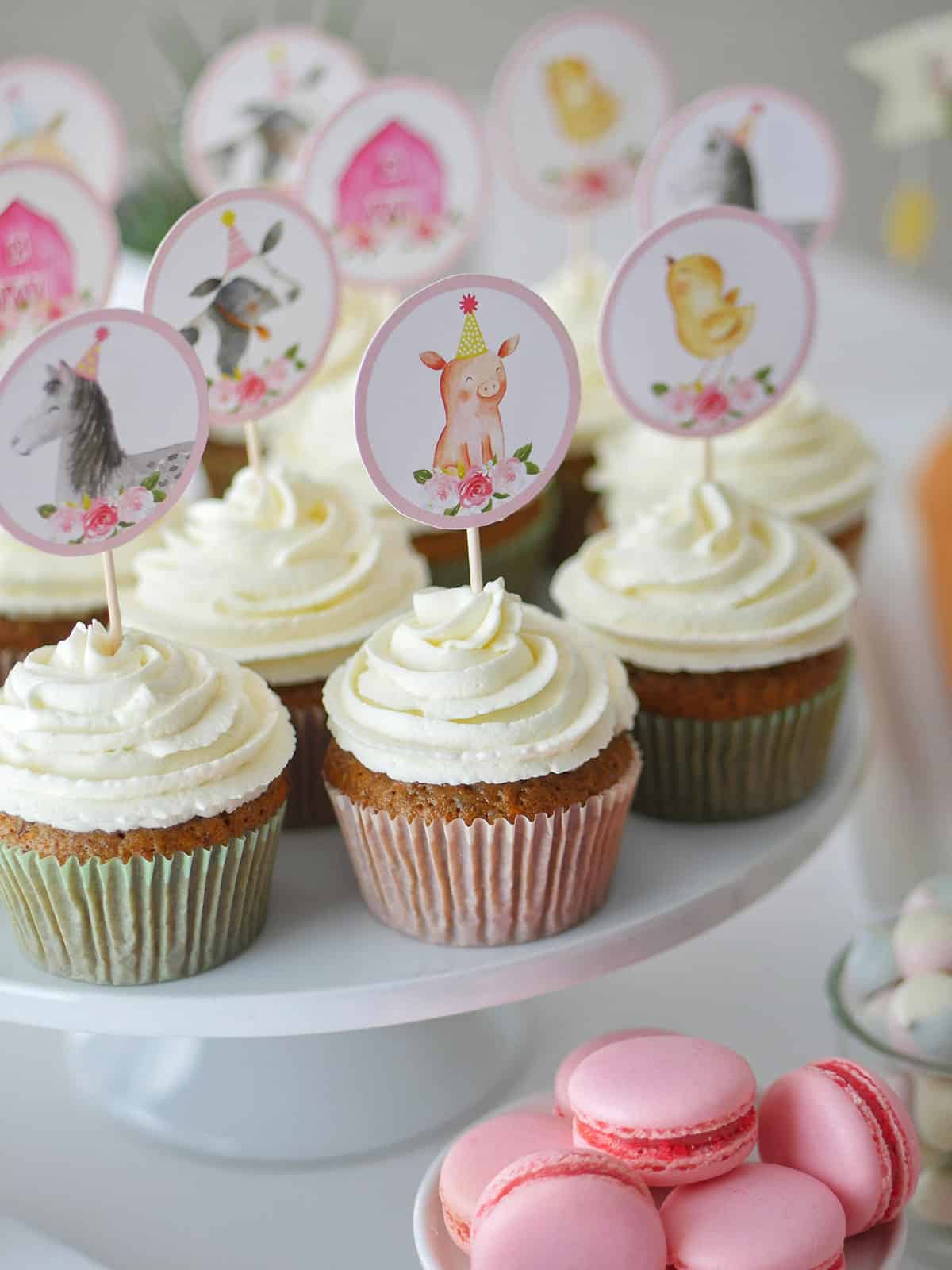 Close up of pecan carrot cupcakes topped with swirls of mascarpone whipped cream and topped with farm animal toppers. 