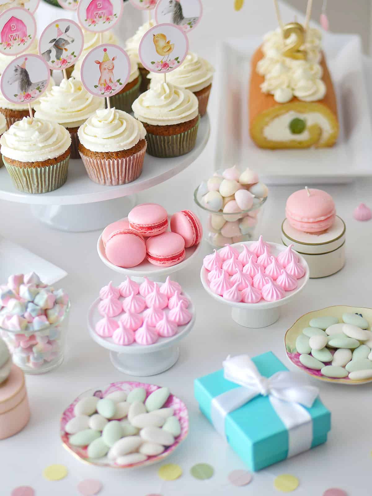 Pink meringue candy styled with other birthday treats like cupcakes and cake logs on a table. 