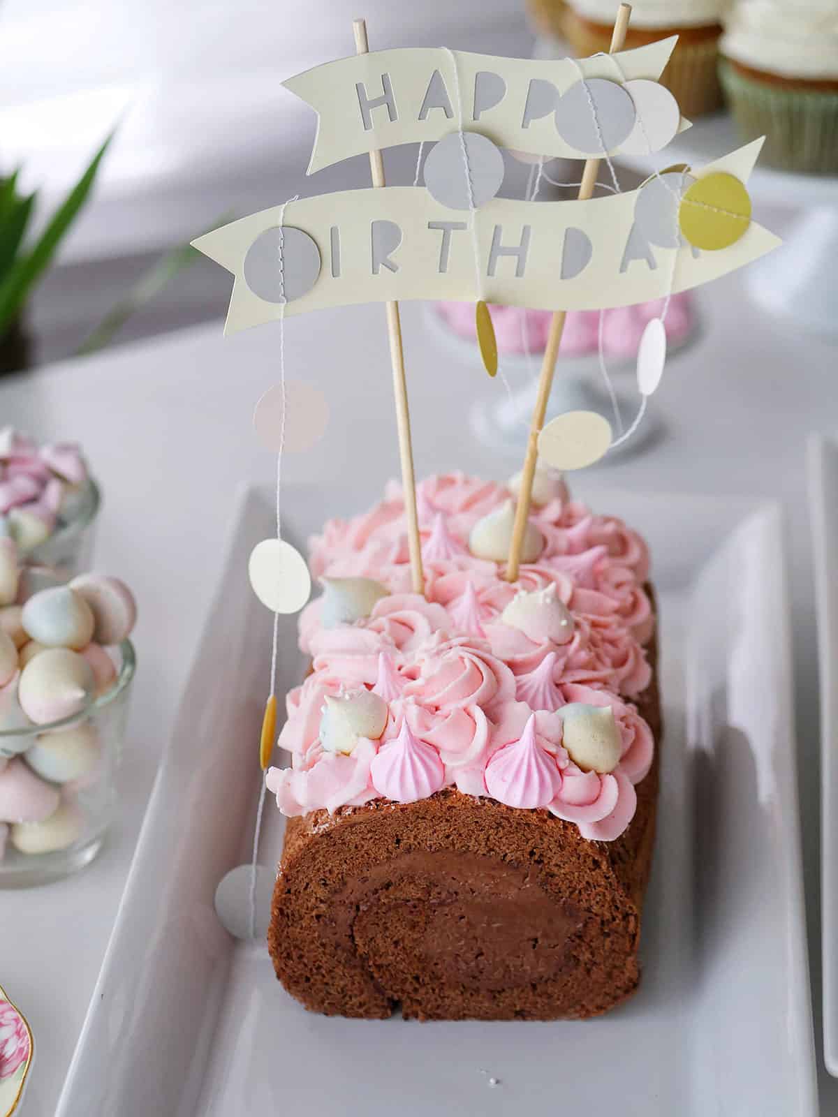 Pink meringue cookies decorating a top of a chocolate cake roll. 