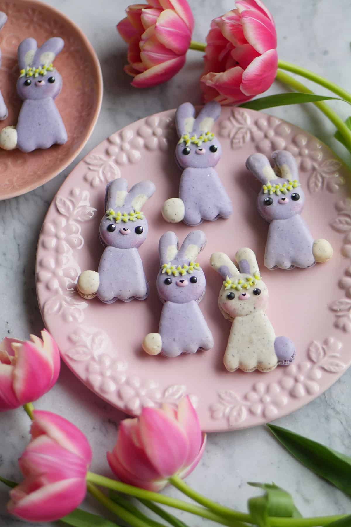A bunch of bunny macarons on a plate surrounded by  flowers.