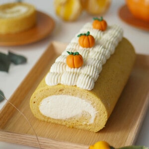 An pumpkin cake roll on a wooden tray with little pumpkins on top with cream.