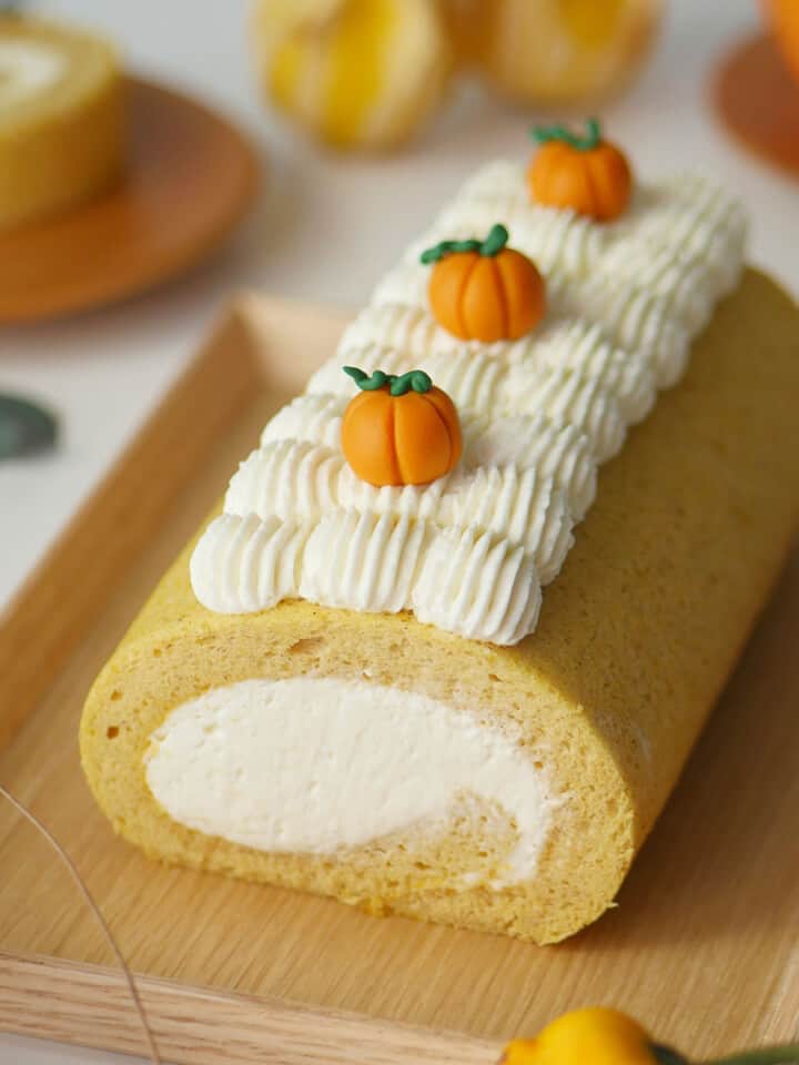 An pumpkin cake roll on a wooden tray with little pumpkins on top with cream.