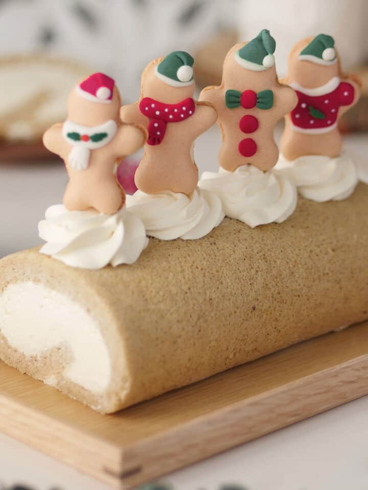 Gingerbread spice cake roll on a wooden tray topped with 4 macaron gingerbreadmen.