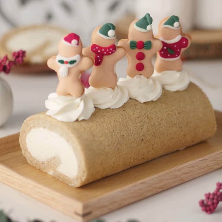 Gingerbread spice cake roll on a wooden tray topped with 4 macaron gingerbreadmen.
