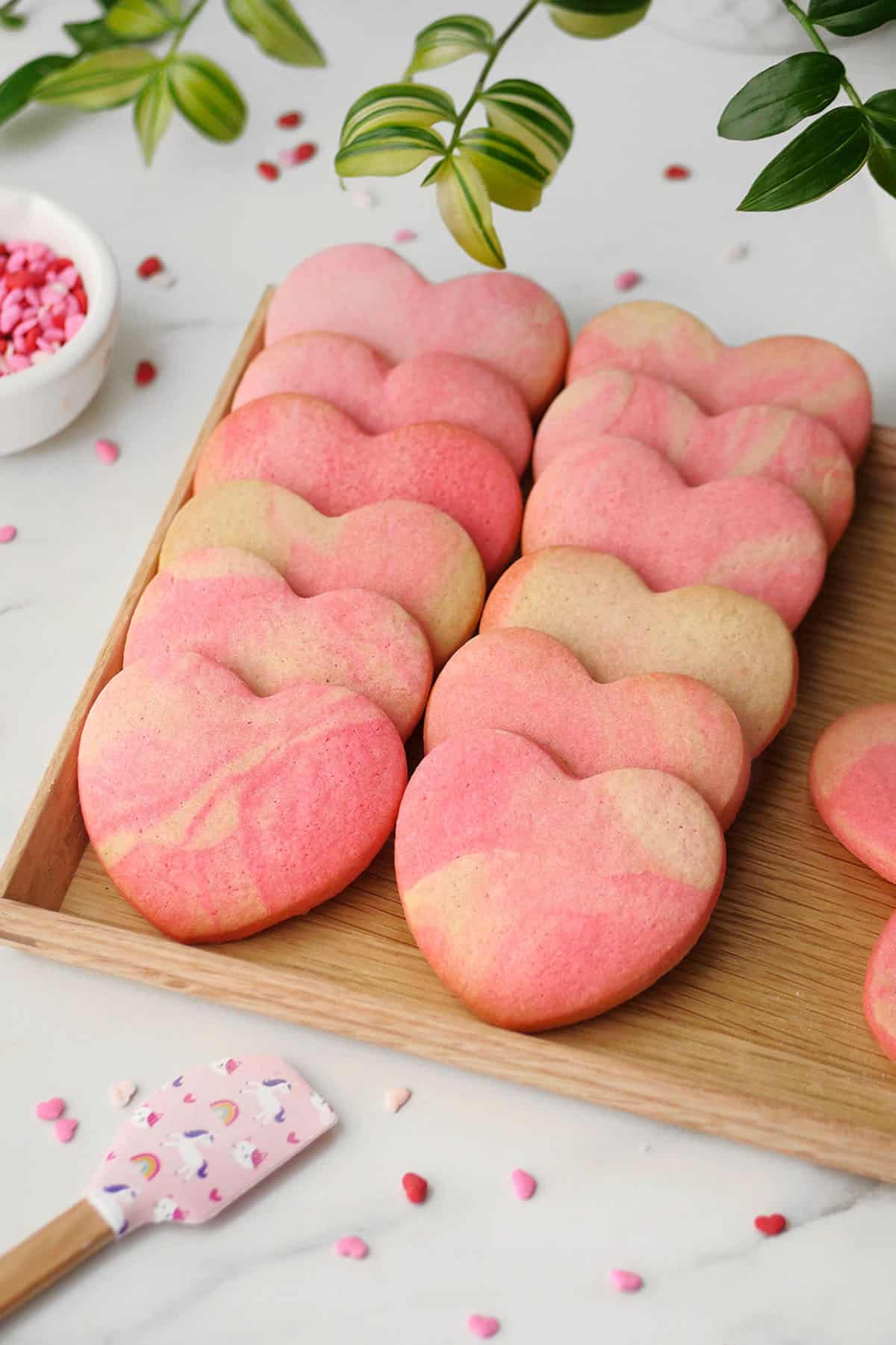 Marbled heart cookies are finished baking and placed onto a wooden tray for serving adorned with heart sprinkles on the side. 