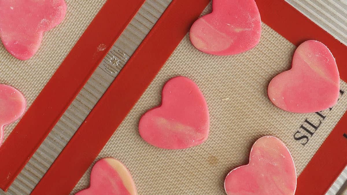 Marbled cookie dough is cut out into a heart shape and placed onto a baking tray. 