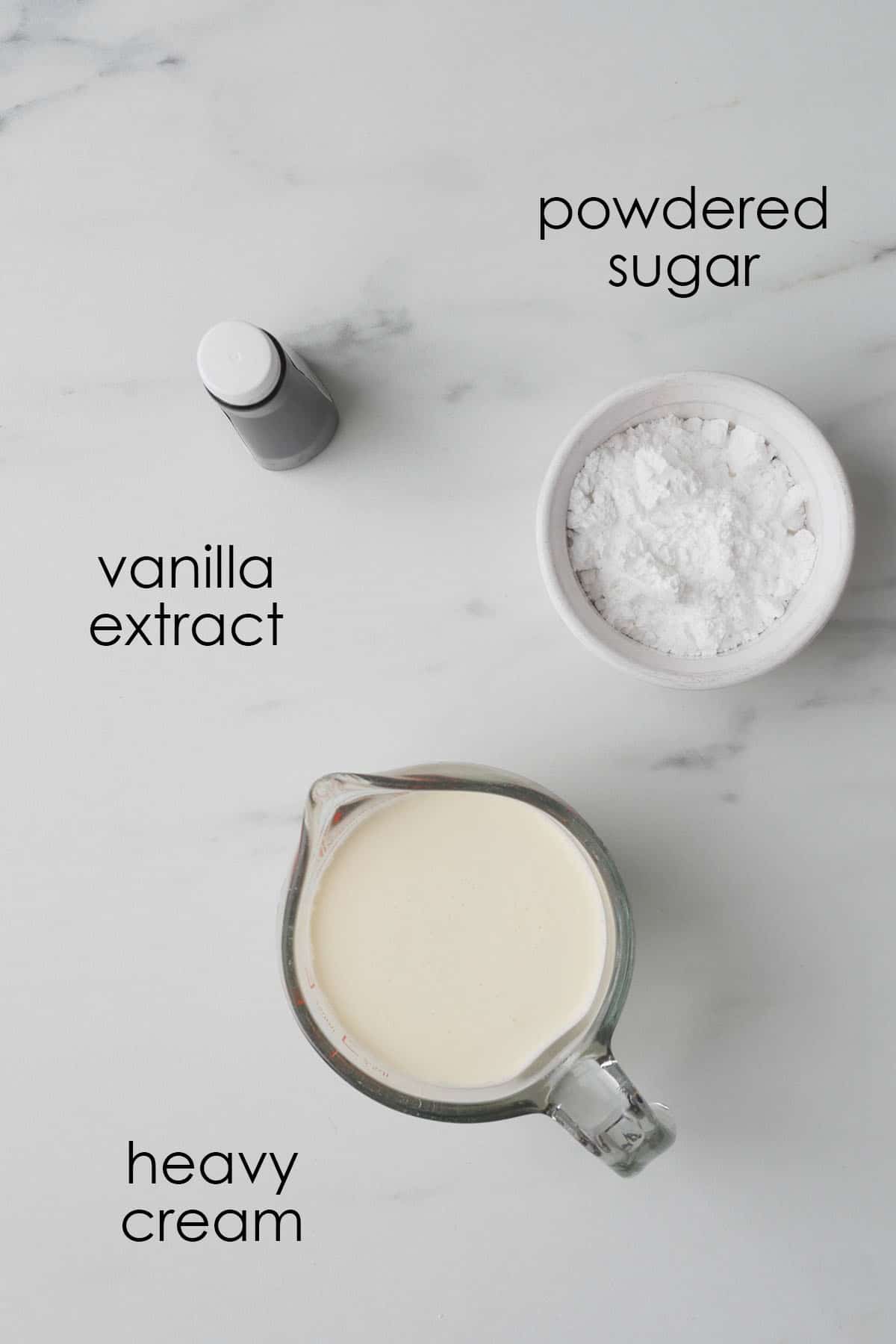 Ingredients for fresh whipped cream laid out on a marbled counter. 