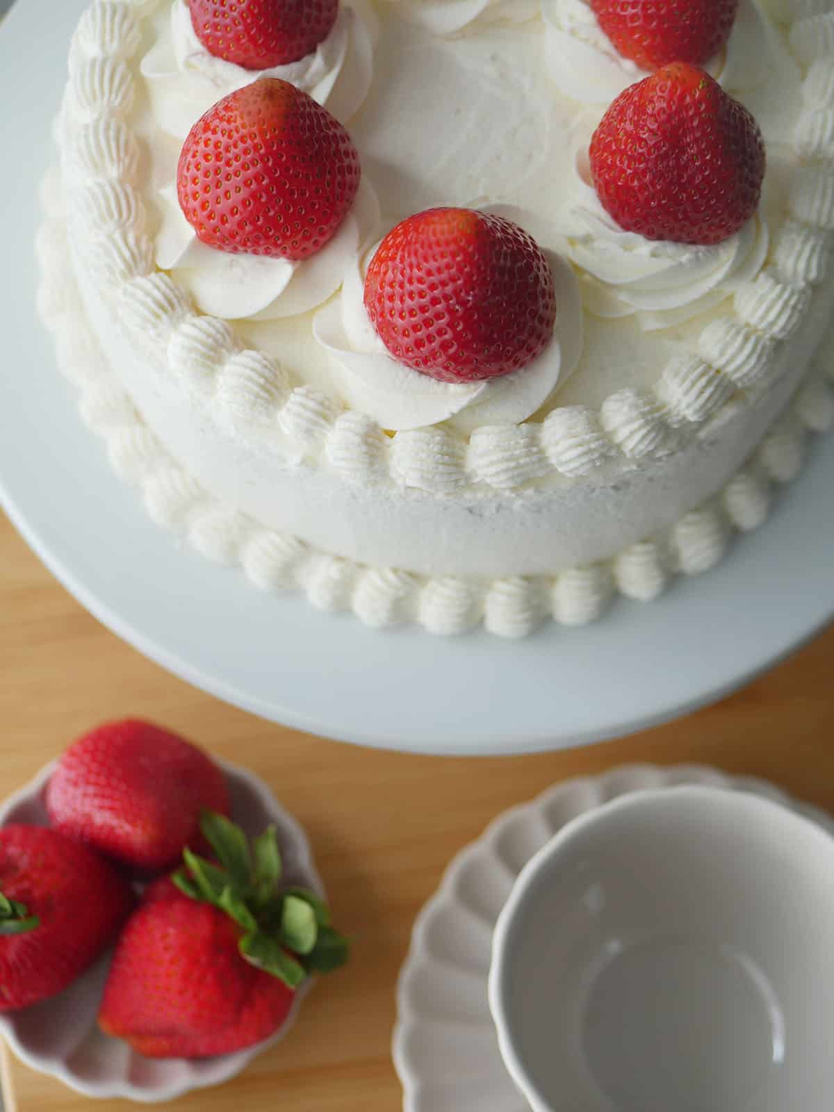 Close of of fresh whipped cream piped into borders on top of a cake topped with strawberries. 