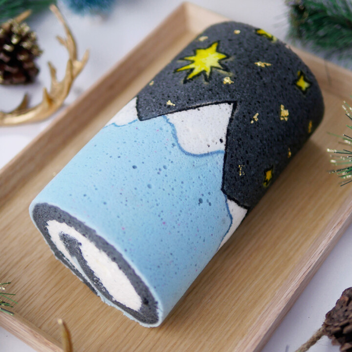 A festive holiday cake roll printed with a mountain and star scene on a wooden serving board.