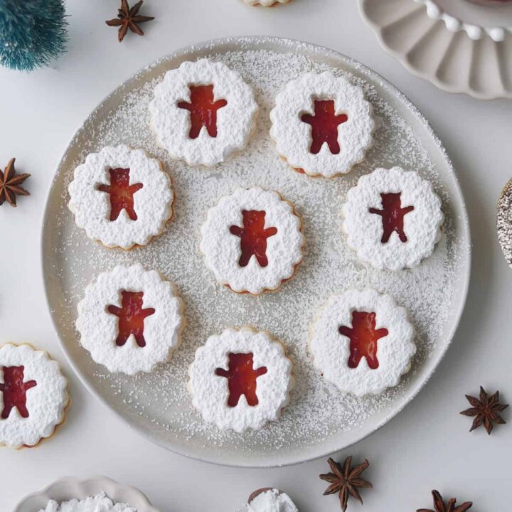 Bear shaped linzer cookies on a round plate flanked by mini Christmas trees.