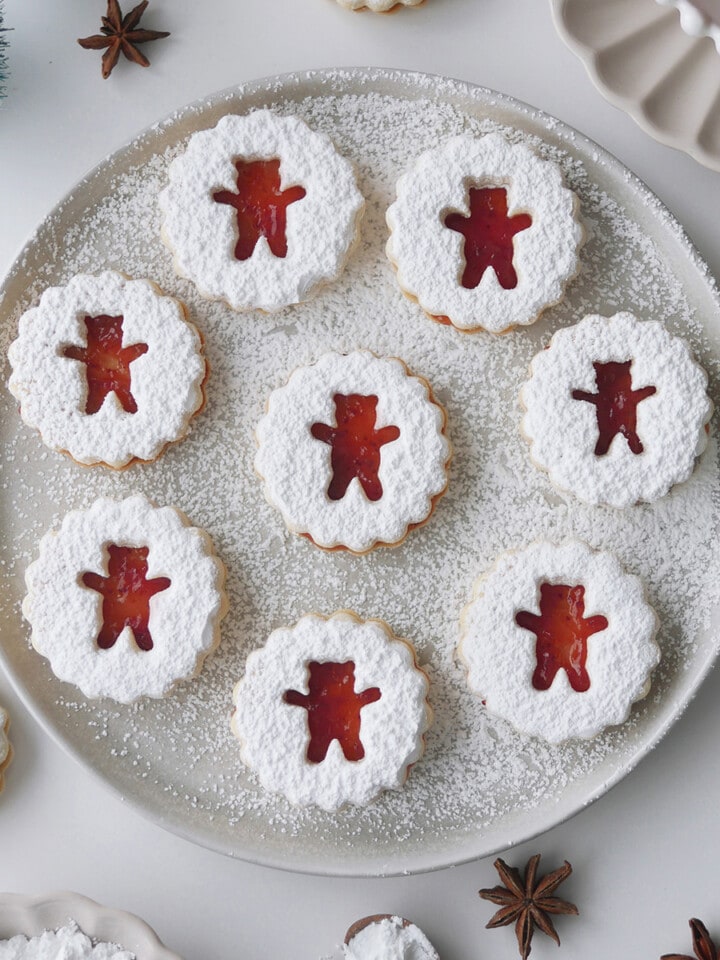 Bear shaped linzer cookies on a round plate flanked by mini Christmas trees.