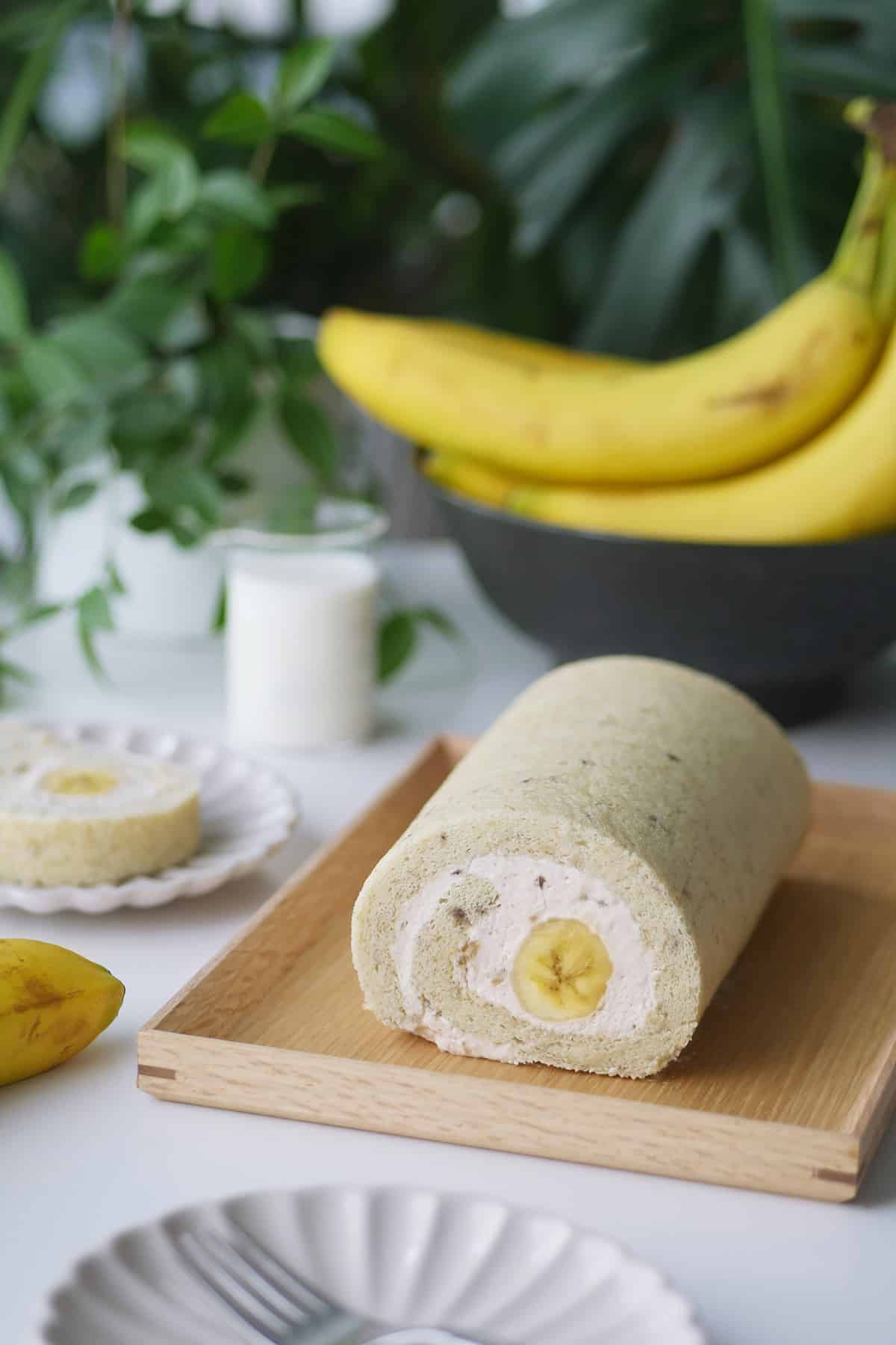 A close up view of a banana cake roll with a piece cut out revealing the cross section of a whole banana inside the roll. 