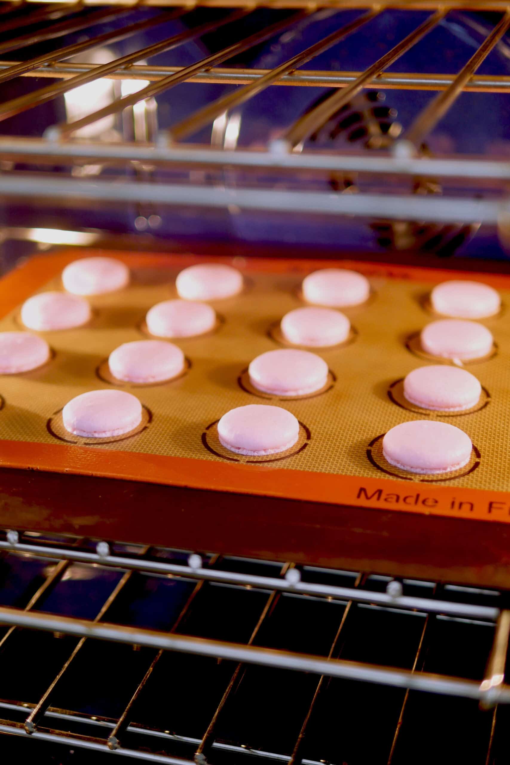 Macarons with small feet being baked in the oven on the middle rack. 
