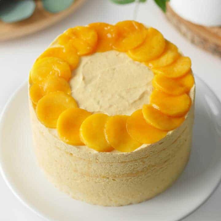 Mango mousse cake on a serving stand topped with fresh slices of mango.