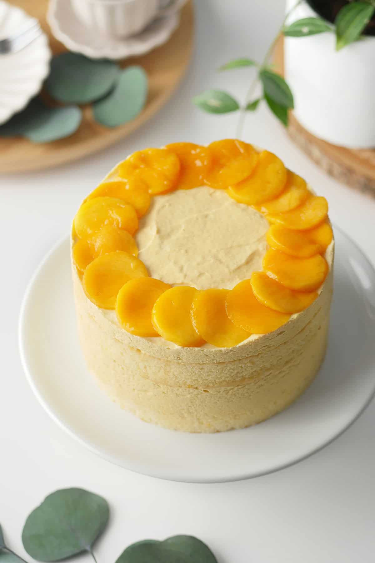 A whole mango mousse cake on a cake stand, it's topped with slices of ripe mangos cut out in a round shape. 