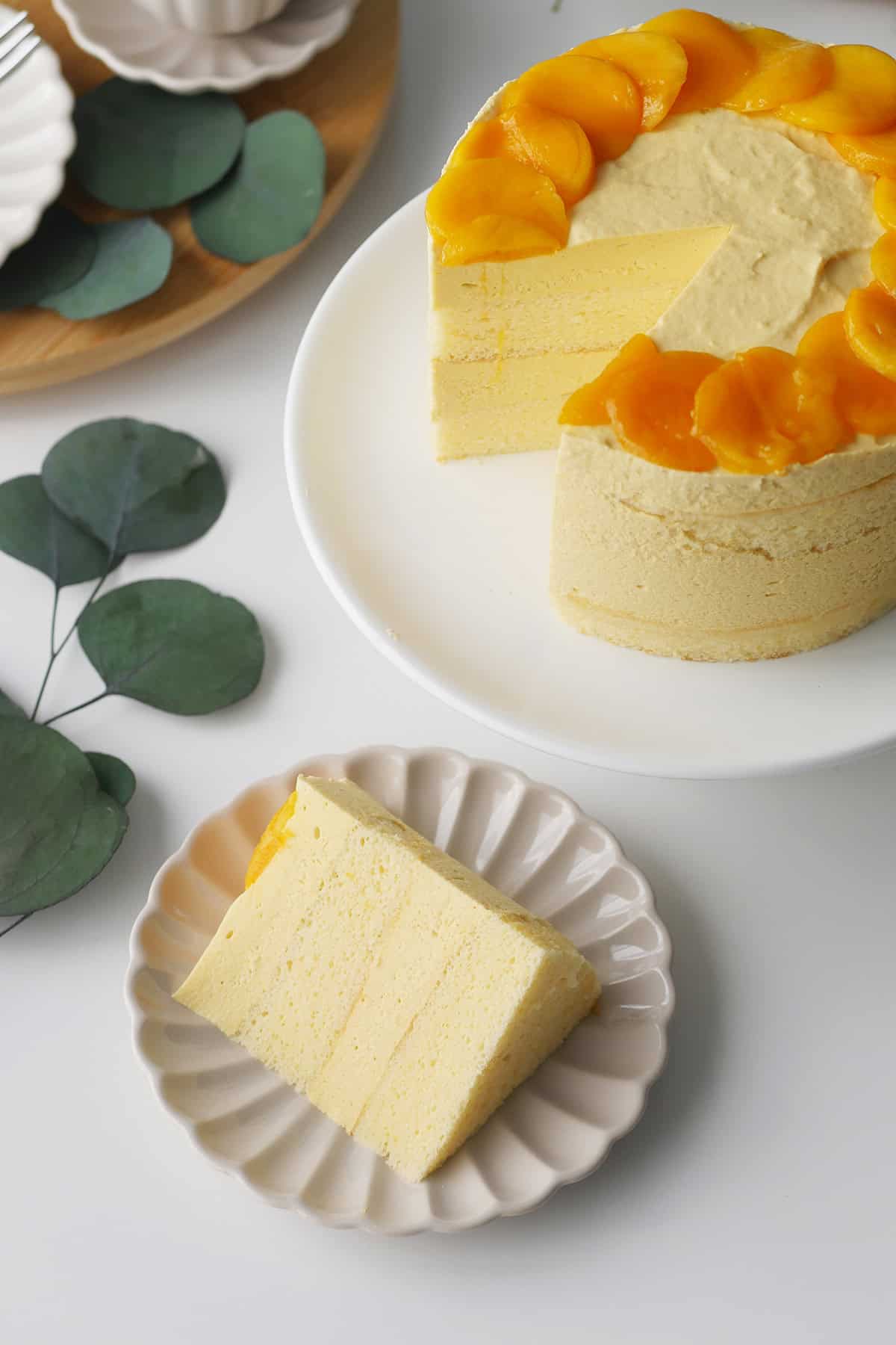 A slice of mango mousse cake is cut out and placed on a plate showing alternating layers of mousse and cake. 