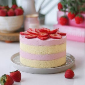 Strawberry mousse cake on a plate with some fresh strawberries in a bowl in the back.
