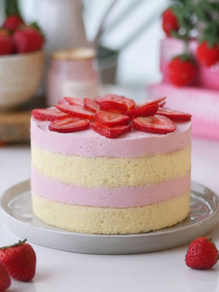 Strawberry mousse cake on a plate with some fresh strawberries in a bowl in the back.