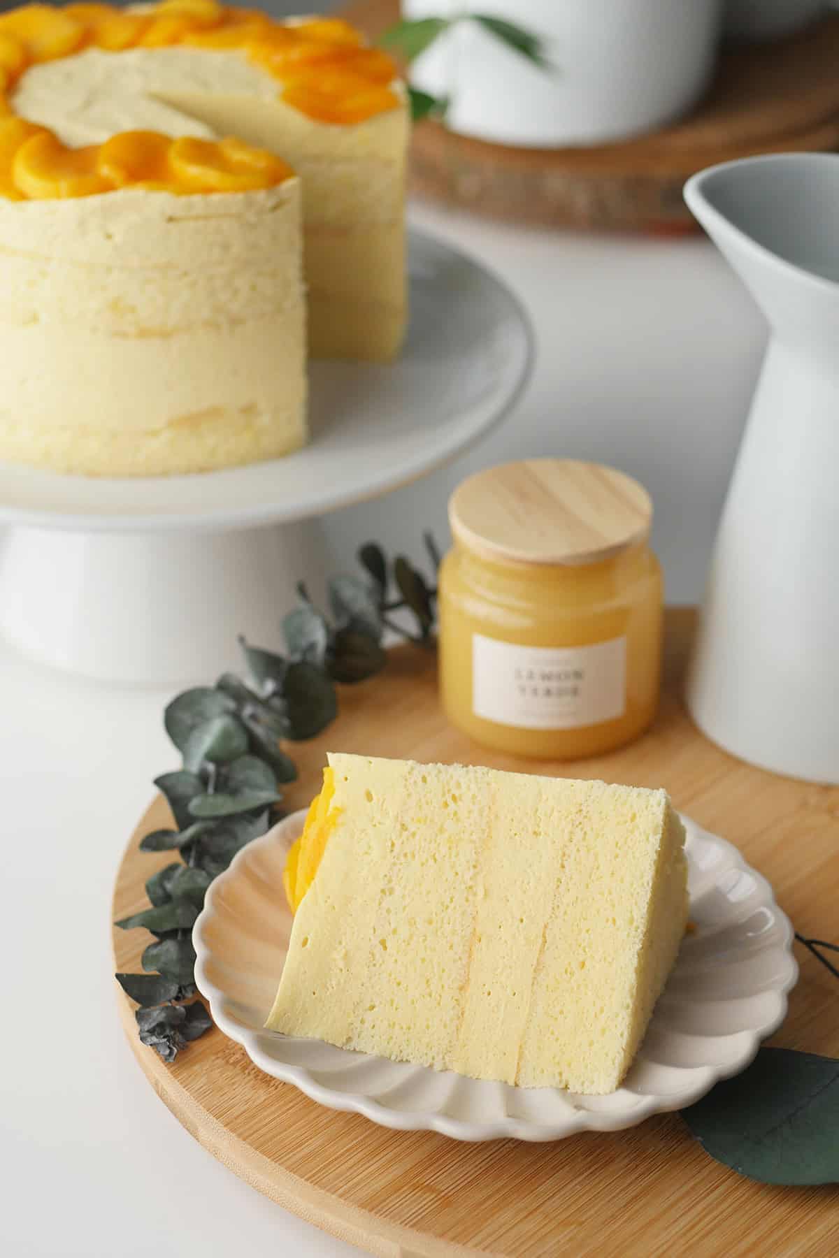 Close up a slice of mango mousse cake on a plate with the whole cake in the background. 