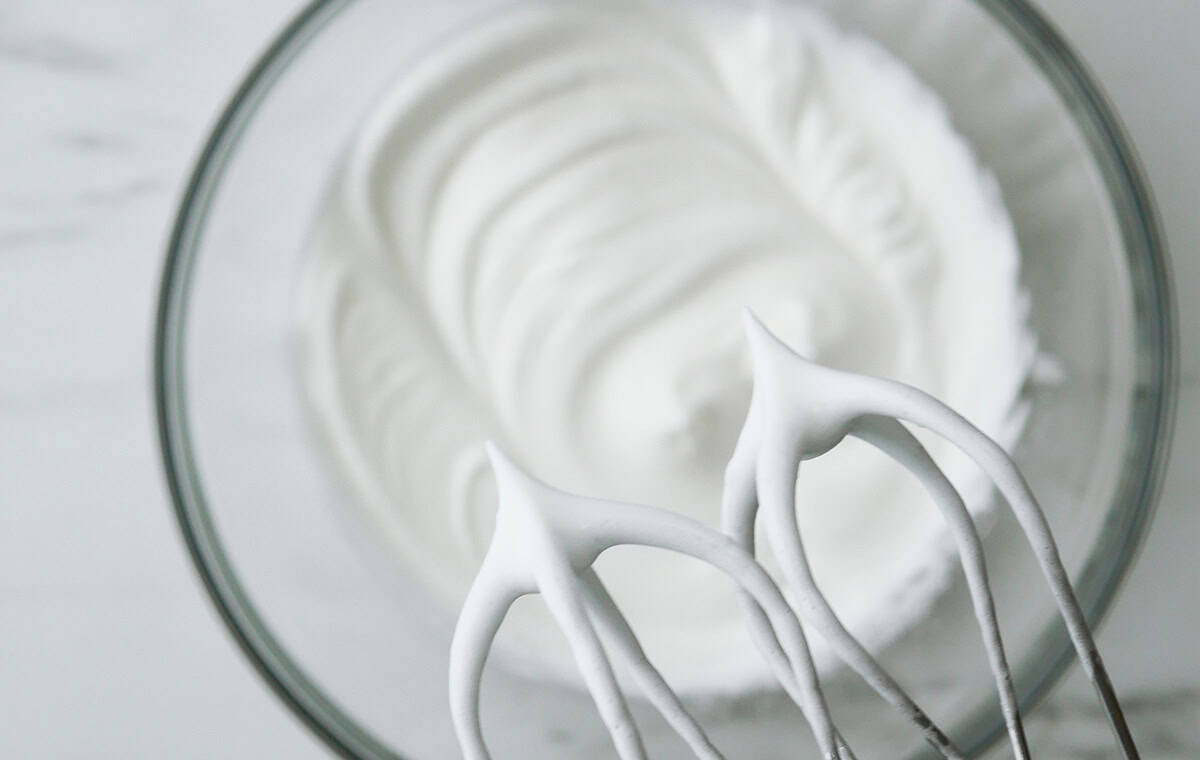 Close up of beaters with meringue on it. The tips of the peaks are standing vertically as it has reached the stiff peaks stage. 