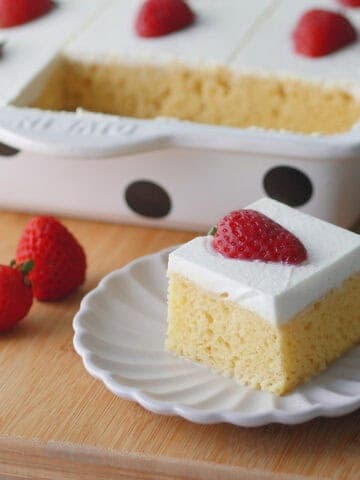 Close up of a slice of tres leches cake showing the fluffy yellow crumbs and white whipped cream frosting.