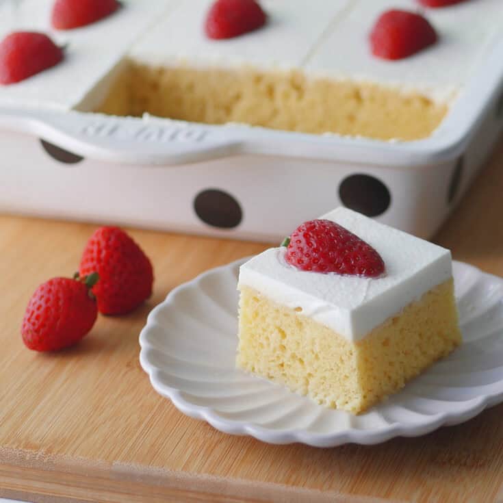 Close up of a slice of tres leches cake showing the fluffy yellow crumbs and white whipped cream frosting.