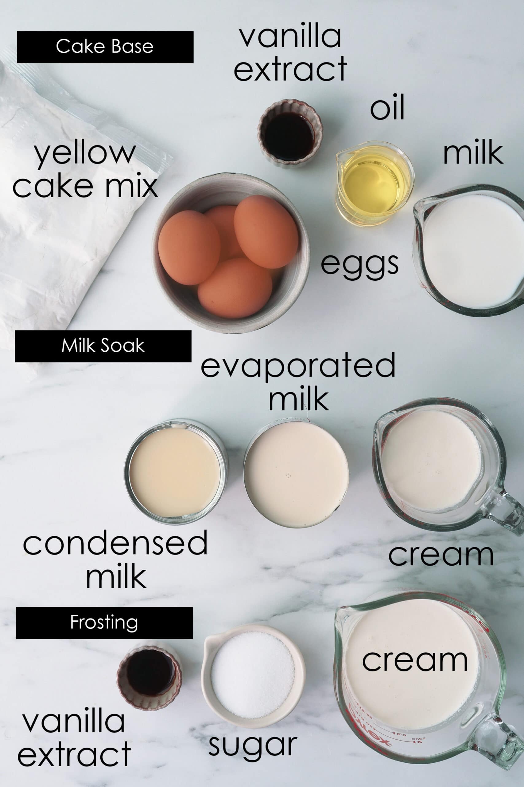 Ingredients for Tres Leches cake in laid out on a marbled counter including a pack of commercial box cake mix. 