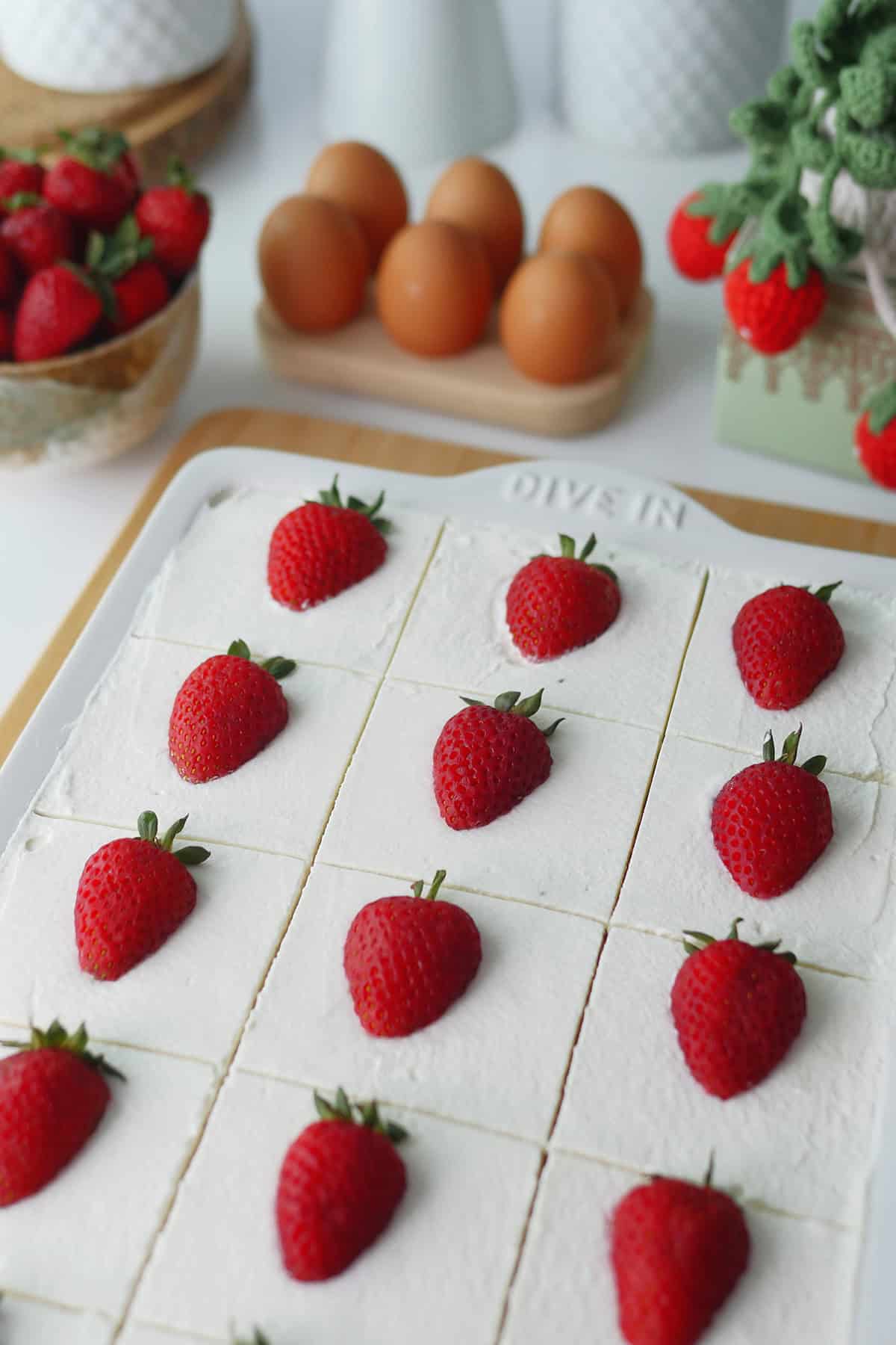 Top down view of Tres Leches cake cut into 12 pieces with perfectly straight lines and topped with fresh strawberries. 