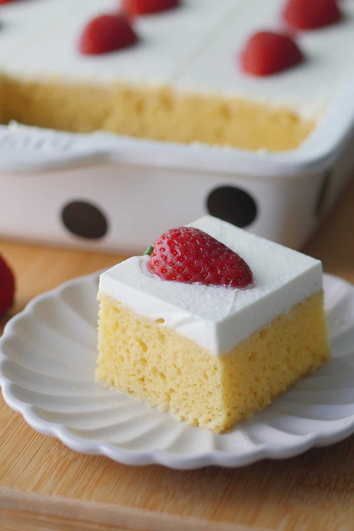 A close up of a piece of tres leches cake showing open crumbs and a little bit of milk pooling on the bottom of the cake. 