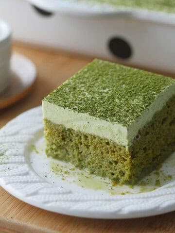 A slice of green tea Tres Leches cake is on a plate with some matcha milk puddling underneath it.