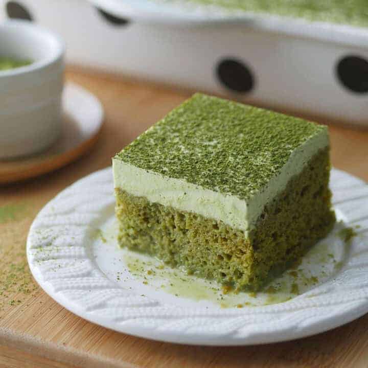 A slice of green tea Tres Leches cake is on a plate with some matcha milk puddling underneath it.