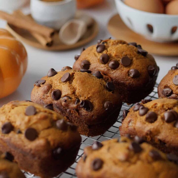 Mini pumpkin spice loaves on a cooling rack with spices and pumpkins in the background.