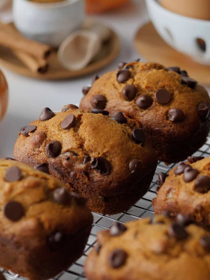 Mini pumpkin spice loaves on a cooling rack with spices and pumpkins in the background.