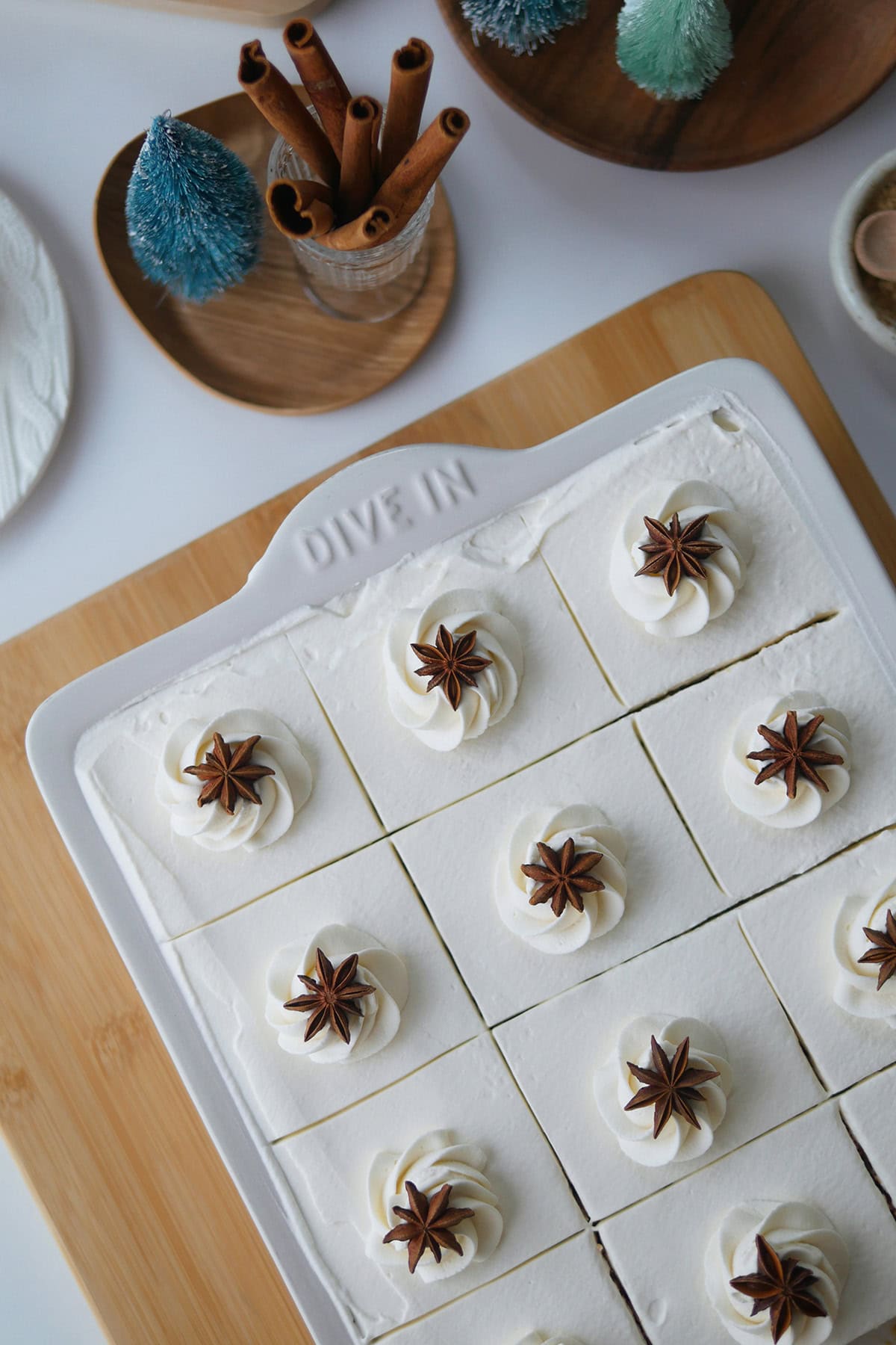 Top down view of Gingerbread Tres Leches cake in a sheet pan shown with some mini bottle brush Christmas trees and cinnamon bark.
