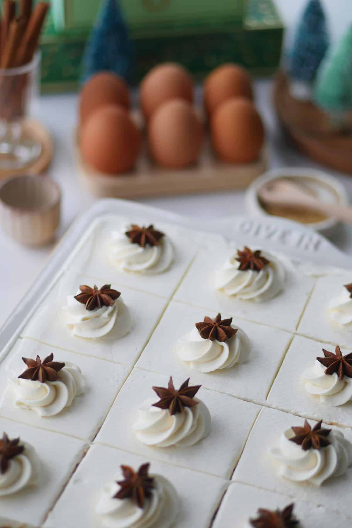 Angled view of the top of a frosted gingerbread tres leches dessert in a rectangular sheet cake pan. The top of the cake is decorated with a swirl of whipped cream frosting and star anise.